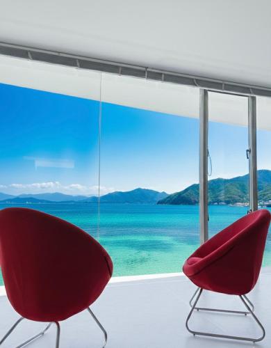 two red chairs in a room with a view of the ocean at Mare di Miyajima マーレ ディ ミヤジマ in Miyajima