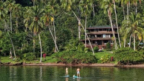 two men on surfboards in the water in front of a resort at Playa Cativo Lodge in Esquinas