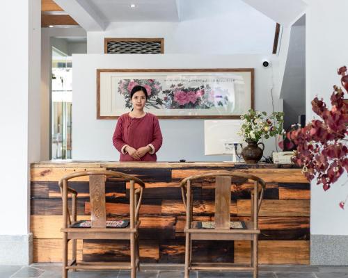 a woman standing behind a wooden bar with two chairs at Guilin Qingshanshe Hotel -Free pick up train station stay two nights in Guilin