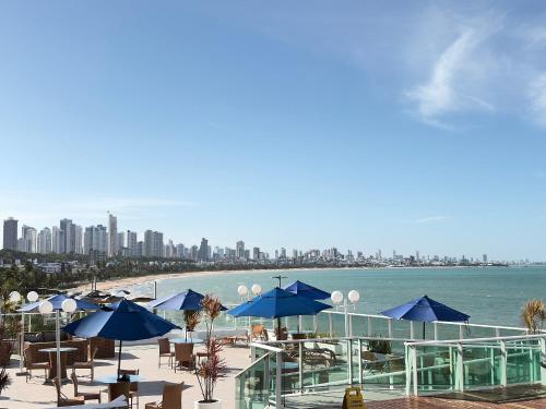 a beach with blue umbrellas and chairs and the ocean at Flat em Cabo Branco - Blue Sunset in João Pessoa