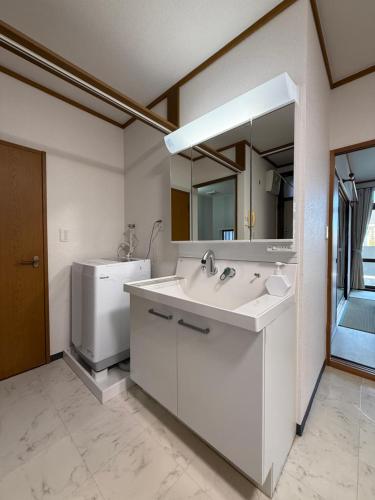a white bathroom with a sink and a mirror at 禅 宮島 一棟貸し 最大6名 ダブルベット3台 2階建の1棟貸しホテル in Hatsukaichi
