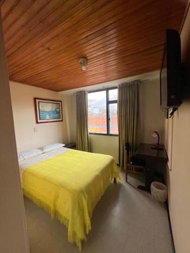 a bedroom with a yellow bed and a window at Hotel Cordillera Real in Sogamoso