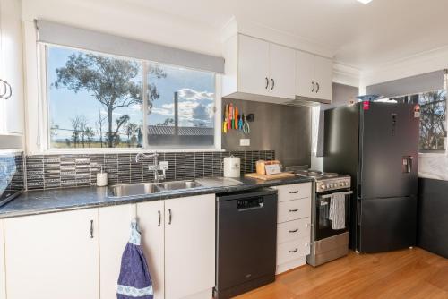 a kitchen with white cabinets and a black refrigerator at Clarendon Cottage, near Lowood , Fernvale, right on the BVRT in Clarendon