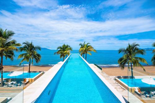 a swimming pool on the beach with palm trees and the ocean at Stunning Beachfront Condo - Sea Views & Pools in Puerto Vallarta