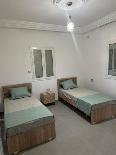 two beds in a white room with two windows at Les jardins de Sara in Mellita