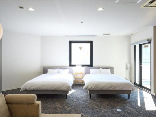 two beds in a room with white walls and windows at Retrospect Stay Kannai in Yokohama