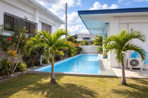 a swimming pool in the yard of a house with palm trees at Machinaka Miyako in Miyako-jima