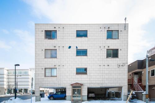 a white brick building with a blue car in front at Silk Court 202 in Chitose