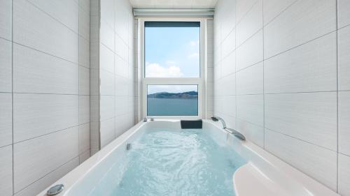a bath tub in a room with a window at Yeosu Jangsuri Poolvilla&Spa Pension in Yeosu