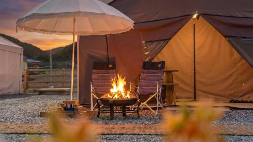 a fire pit in front of a tent with two chairs and an umbrella at Gapyeong ILUGlamping in Gapyeong