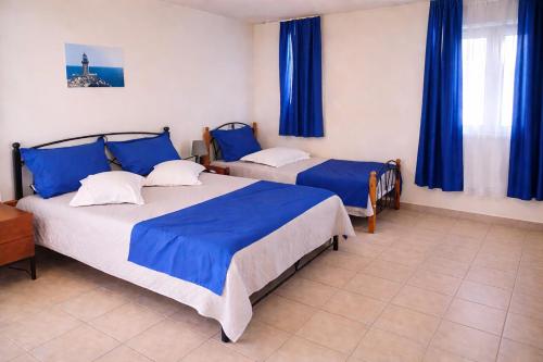 two beds in a room with blue curtains at Apartments Hotel & Studios, Xifoupolis in Monemvasia