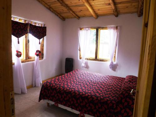 a bedroom with a bed and two windows at Complejo Turístico Sol de Puelo in Lago Puelo