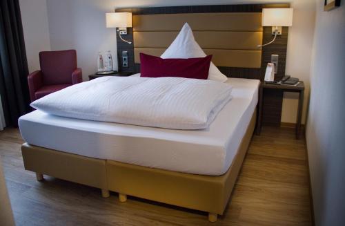 a bedroom with a bed with white sheets and red pillows at Hotel Restaurant Passmann in Lüdenscheid