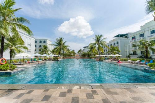 a large swimming pool with palm trees and buildings at Leono Coast Beach Hotel Phu Quoc in Phú Quốc