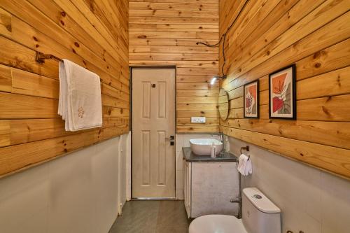 a bathroom with wooden walls and a toilet and a sink at SaffronStays Anjee's Chalet in Dhamni