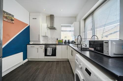 a kitchen with white cabinets and a large window at Six Bedroom Group Home near MediaCityUK with Garden and Lockbox Check In in Manchester