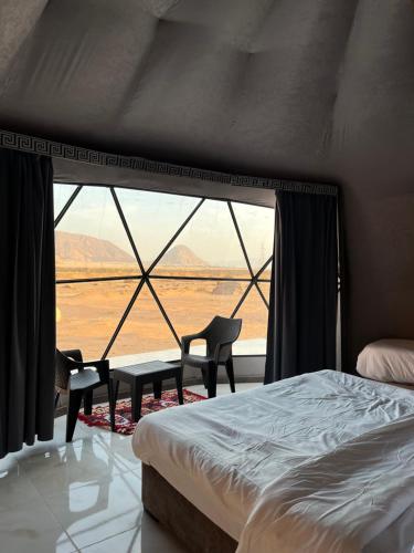 a bedroom with a bed and two chairs and a large window at The Martian Bubbles - Wadi Rum in Wadi Rum