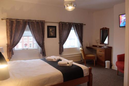 a bedroom with a bed and a desk and two windows at Yarm View Guest House and Cottages in Yarm