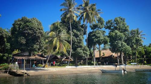 a beach with palm trees and a boat in the water at Pristine Paradise Dive Resort - Togean Islands, Una Una in Pulau Unauna