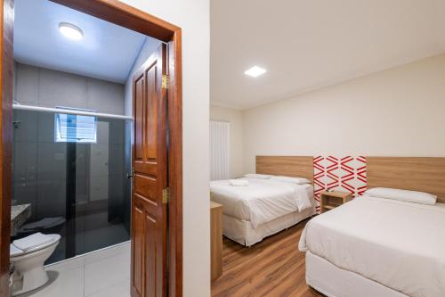 a bedroom with two beds and a bathroom with a toilet at Vektor Hotéis - Unidade Mariana in Mariana