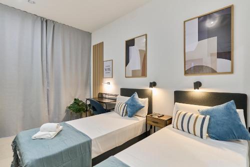 two beds in a hotel room with blue pillows at Sant Adrià Urban Suites by gaiarooms in Badalona