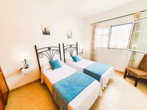two beds in a room with a chair and a window at Apartamentos Graciosamar in Caleta de Sebo