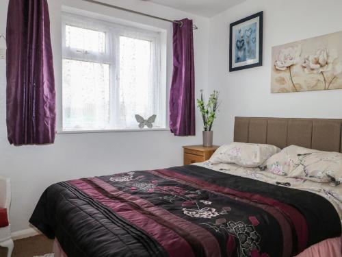 a bedroom with a bed and a window with purple curtains at 90 Bay View in New Romney