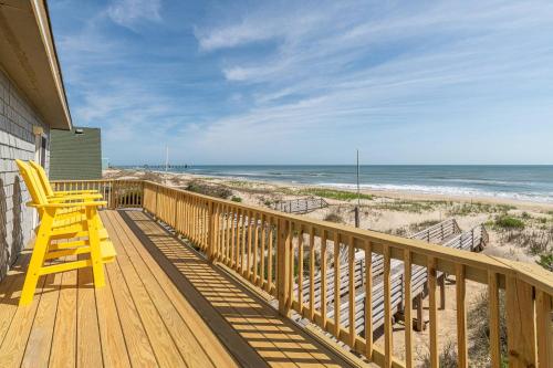 a yellow chair sitting on a deck looking at the beach at Pier Pleasure - S Nags Head MP 17, Oceanfront, Private Beach Access, Ocean View, Fireplace in Whalebone