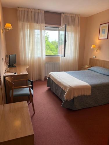 a hotel room with a bed and a desk and a window at Hotel Restaurante La Alhama in Medina de Pomar