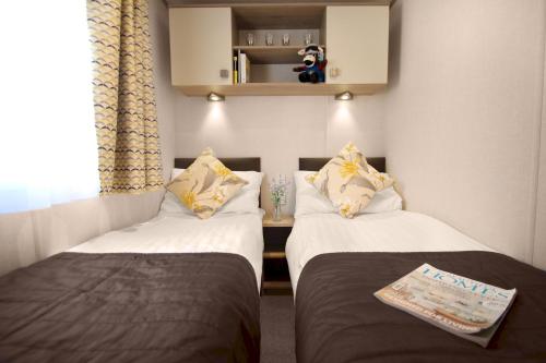 two twin beds in a small room with a window at 2. Supreme OD 2 Caravan with Decking in Ringwood