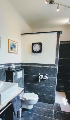 a bathroom with a toilet and a clock on the wall at La Porte Noire in Courcelles
