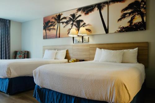two beds in a hotel room with palm trees on the wall at Days Inn by Wyndham Anaheim Near the Park in Anaheim
