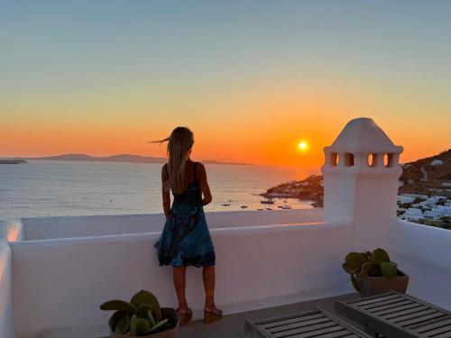 a woman standing on a ledge looking out at the sunset at Villa Vanita Agios Ioannis Mykonos in Agios Ioannis Mykonos