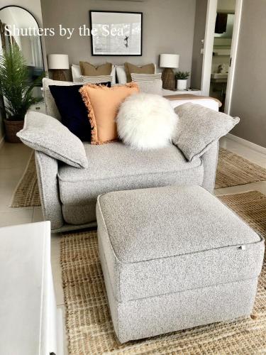 a couch with pillows and a ottoman in a living room at Shutters Hamptons Hideaway with Sea view-Waterfront in Kiama