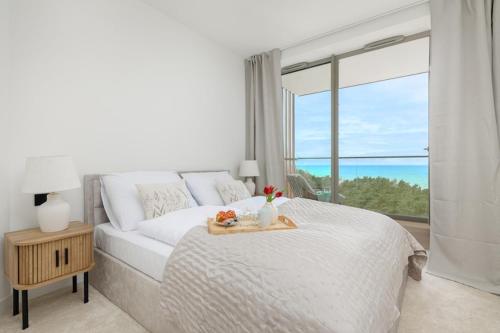 a white bedroom with a bed and a large window at Apartment with direct sea view in Pobierowo