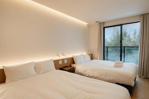 two beds in a room with a window at MIRATIO Umui Sauna&Spa in Onna