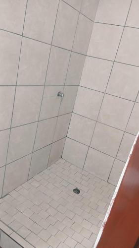 a bathroom with a shower with white tiled floors at THEMBAGUESTHOUSe in Benoni