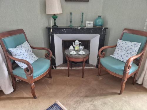 two chairs and a table in a room with a fireplace at Le manoir d'Estiveaux in Le Châtelet