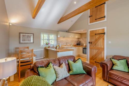 a living room with two leather couches and a kitchen at The Gate Lodge - Pet Free - Near Finchingfield & Saffron Walden in Great Sampford