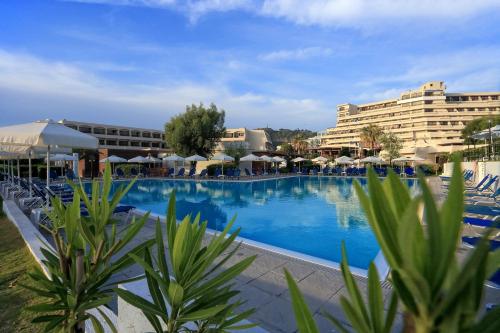 a large swimming pool with chairs and umbrellas and buildings at Sol Cosmopolitan Rhodes in Ixia