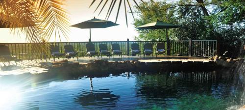 a pool of water with chairs and umbrellas at Victoria Falls Safari Lodge in Victoria Falls