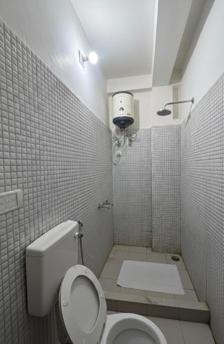 a white tiled bathroom with a toilet and a shower at Mahajan Lodge in Katra