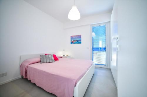 a white bedroom with a pink bed and a window at Villa Almaris in Marina di Ragusa