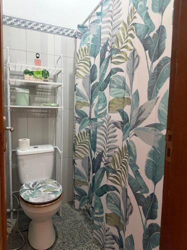 a bathroom with a toilet with a leafy shower curtain at Rahayu House in Kusamba
