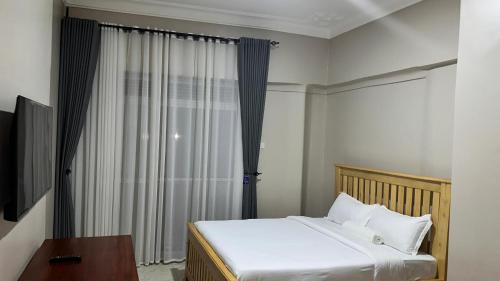 a bedroom with a bed with white sheets and a window at Kuri hotel Kampala in Kampala