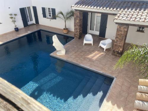 a swimming pool with two white chairs next to a house at Le Patio Bleu in La Crau