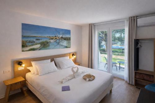 a bedroom with a large bed and a large window at Artemia Aigues-Mortes - Hôtel avec piscine - Bornes électriques - Parking privé - Local vélo-moto in Aigues-Mortes