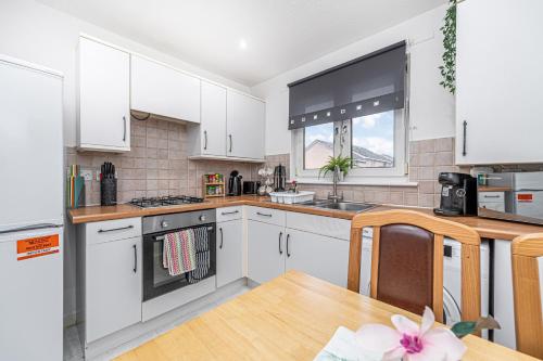 a kitchen with white cabinets and a wooden table at Prime Commuter Executive Apartment Dunfermline in Dunfermline