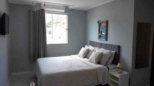 a bedroom with a bed with white sheets and a window at Canoa dos Anjos Suites in Arraial do Cabo