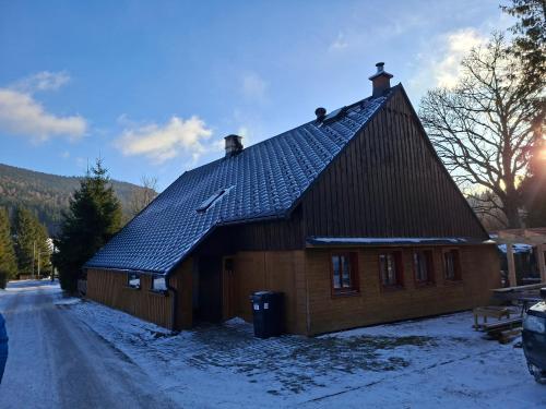 a wooden house with a black roof in the snow at Chalupa Rumovka in Ostružná